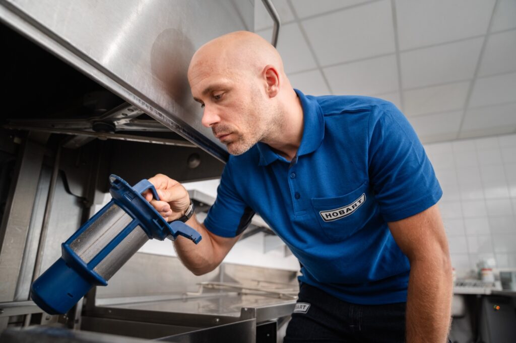 HOBART monteur neemt de filterzeef uit een vaatwasmachine tijdens een controlebeurt