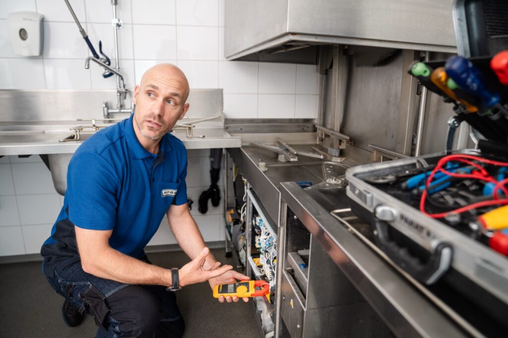 HOBART servicemonteur meet een vaatwasmachine door tijdens een reparatie